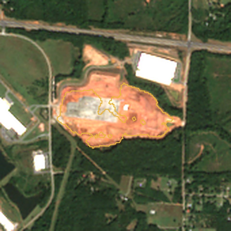 Satellite view in October 2026: 57 acres of bare red clay with a large new pad, outlined in gold